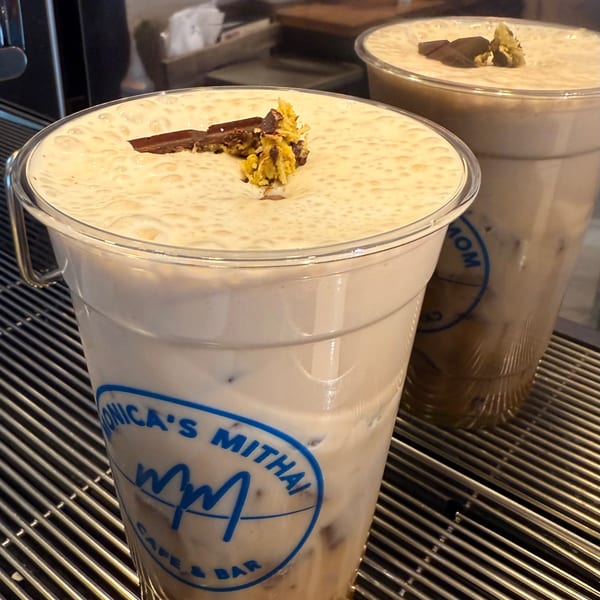Two Monica's Mithai Cafe & Bar iced coffees with foam, chocolate, and nuts on a metal grate.