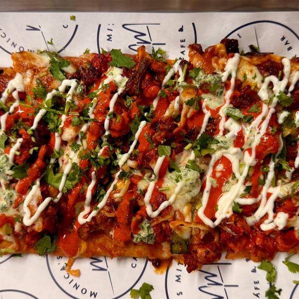 Indian flatbread pizza with chicken tikka, cilantro, and white and green sauces on Monica's branded paper.