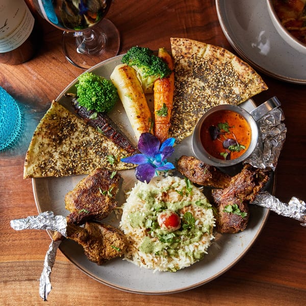 Indian platter with lamb chops, rice, naan, roasted vegetables, and a side of curry.