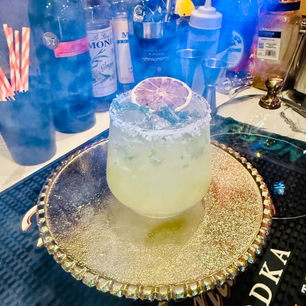 A vibrant yellow cocktail with a salted rim and dried citrus garnish on a gold tray at Monica's Mithai Cafe & Bar.