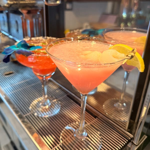 Two pink cocktails, one garnished with lychee and lemon, the other with a blue orchid.