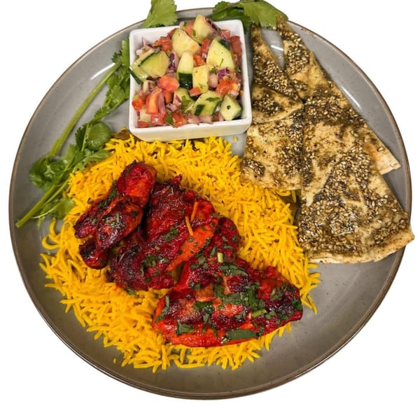 Indian dish with red chicken pieces on yellow rice, a side salad, and flatbread on a gray plate.