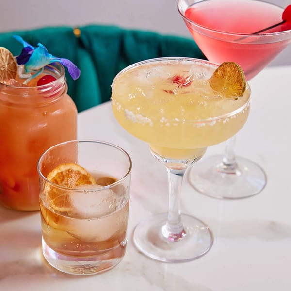 Three colorful cocktails, including a margarita and a martini, on a white marble table.