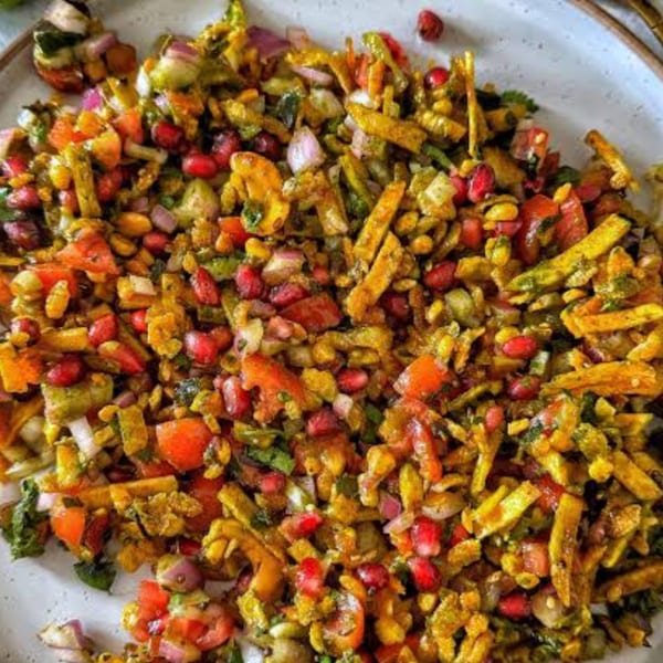 Close-up of a colorful Indian chaat dish with pomegranate, tomatoes, onions, and crispy noodles.