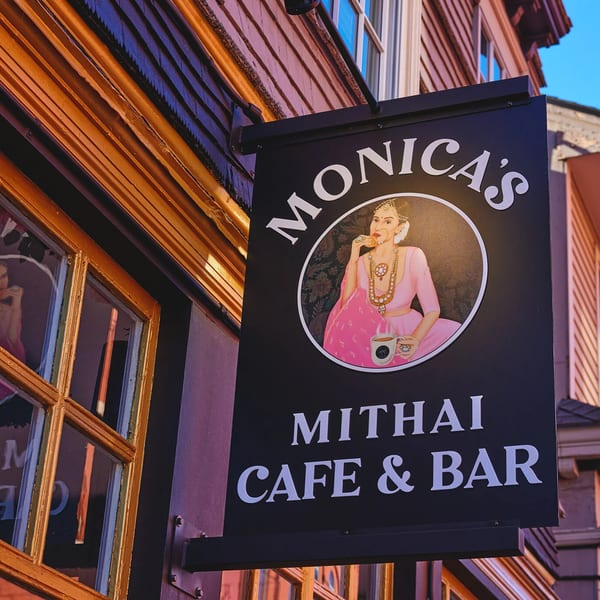 Monica's Mithai Cafe & Bar sign with an Indian woman enjoying a sweet and chai.