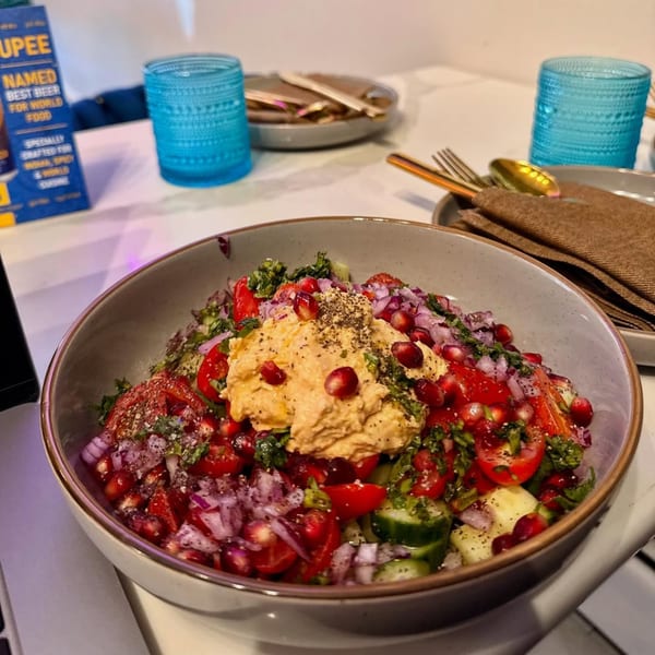 A vibrant Indian salad with hummus, pomegranate, tomatoes, and red onions in a bowl.