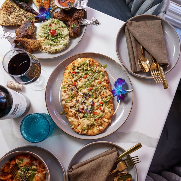 Overhead view of Indian dishes, including naan, rice, chicken, pasta, and a flatbread, with wine.
