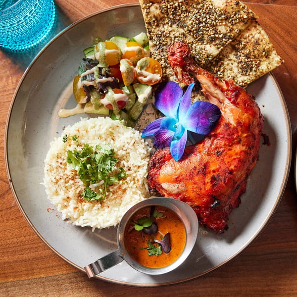 Indian chicken dish with rice, salad, flatbread, and sauce, garnished with a purple orchid.