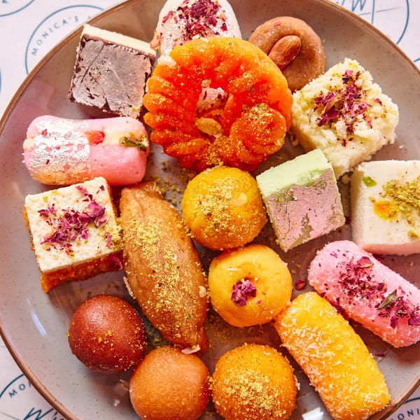 A plate of colorful Indian mithai, including gulab jamun, barfi, and jalebi, garnished with nuts and rose petals.
