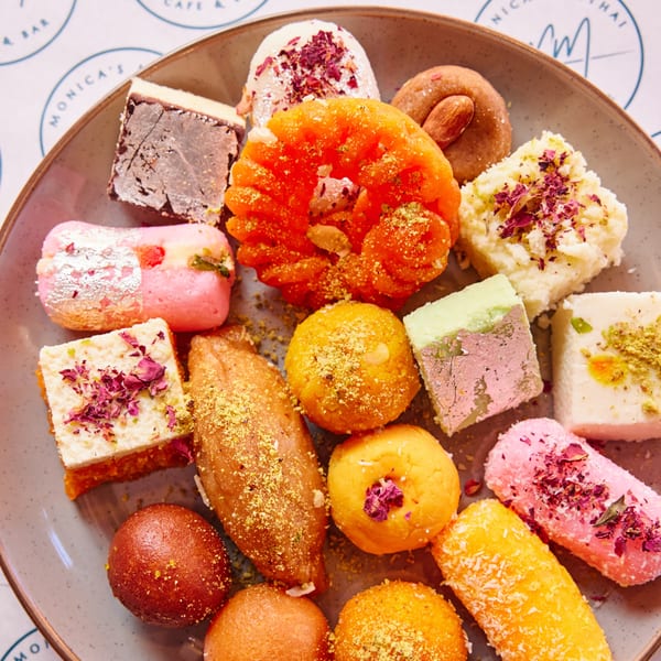 A close-up of a variety of colorful Indian mithai (sweets) on a gray plate.