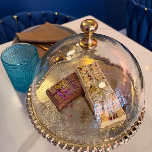 Two Indian mithai chocolate bars, one white and one milk, under a glass cloche on a silver tray.