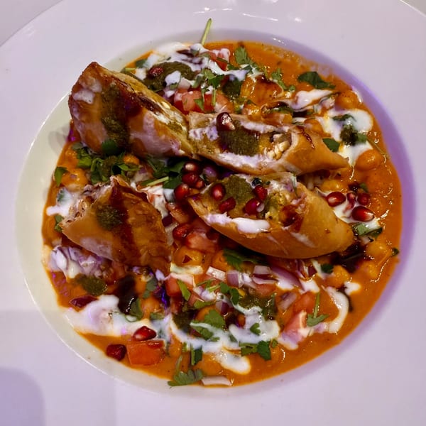 Indian samosa chaat with yogurt, chutneys, pomegranate seeds, and cilantro in a white bowl.