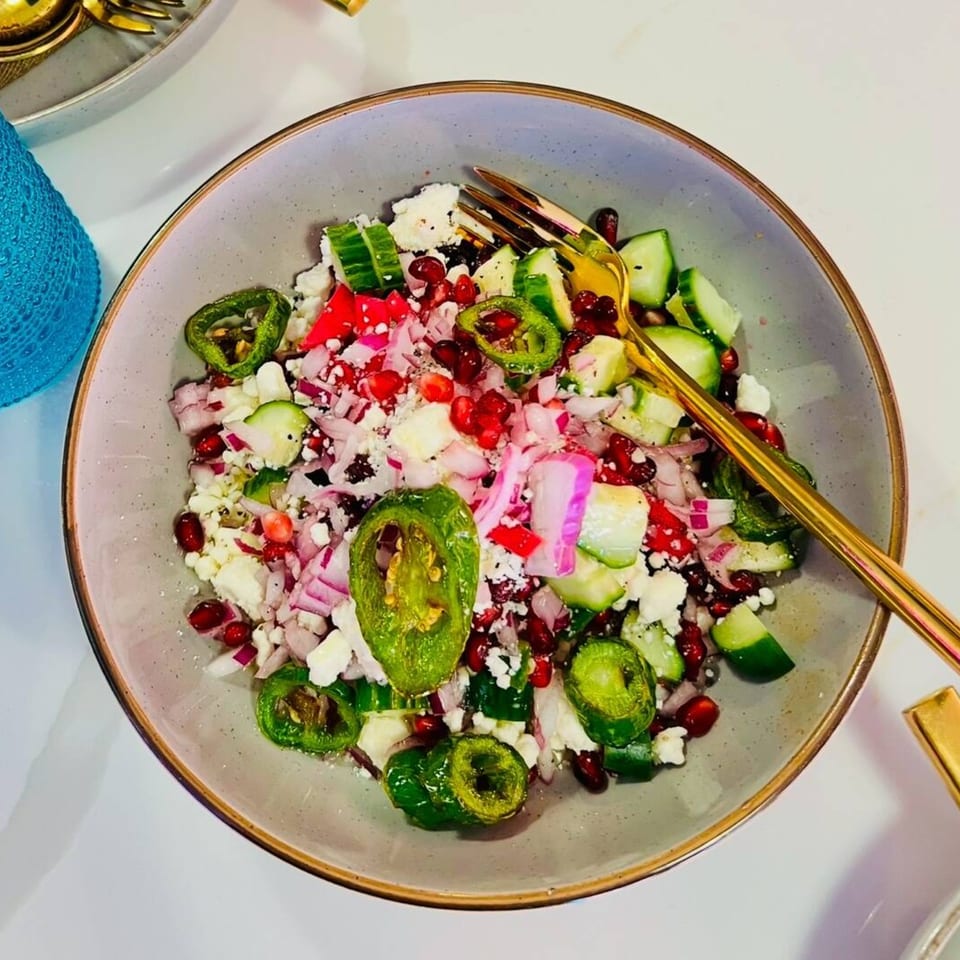 A vibrant Indian salad with cucumbers, red onions, feta, pomegranate seeds, and green chilies.