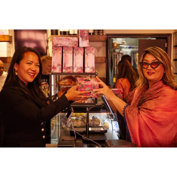 Two women exchanging a pink patterned box of mithai at Monica's Mithai Cafe & Bar.