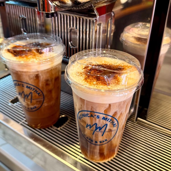 Two iced chai lattes with Monica's Mithai Cafe & Bar logo on a metal grate.