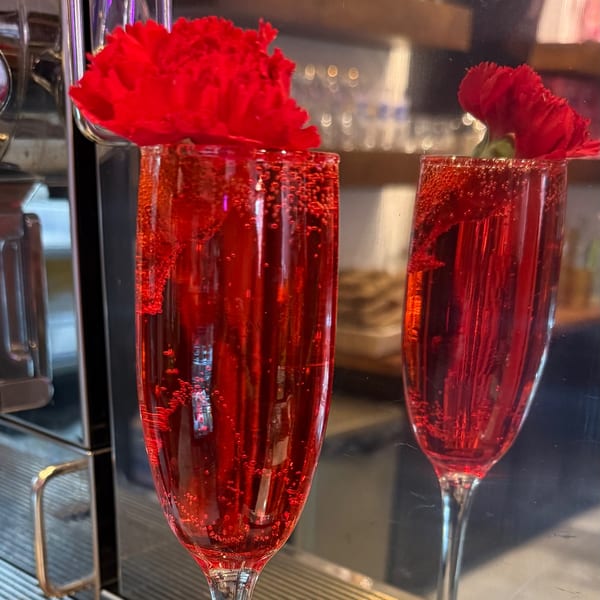 Two flutes of sparkling red drink, garnished with red carnations, at Monica’s Mithai Cafe & Bar.