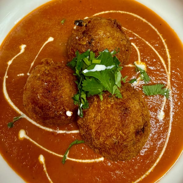 Three golden-brown Indian kofta balls in a rich orange curry, garnished with fresh cilantro and cream swirls.