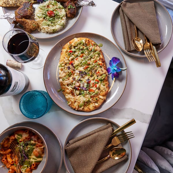 Overhead view of an Indian feast with naan pizza, rice, lamb chops, pasta, and wine.